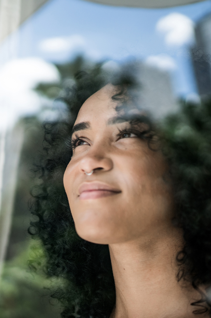 Young woman looking through window at home